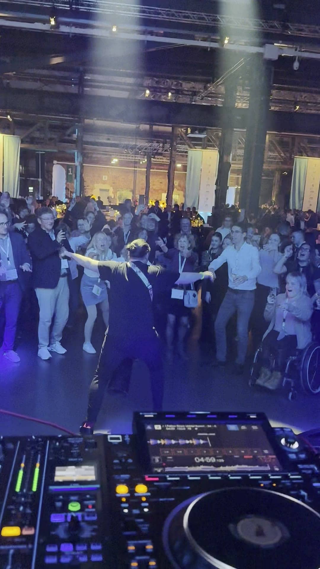 Blick vom DJ-Pult in eine volle Halle: Gäste mit Namensbändern tanzen