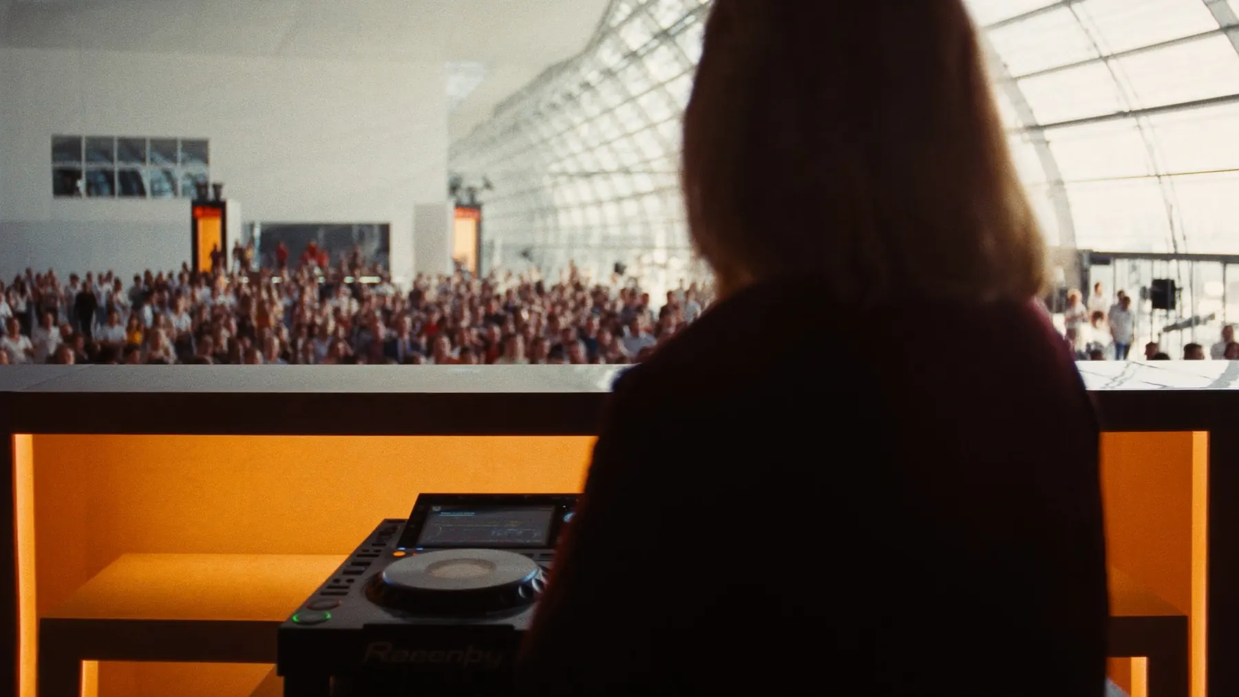 DJ-Booth mit Blick auf eine helle Messehalle und Crowd